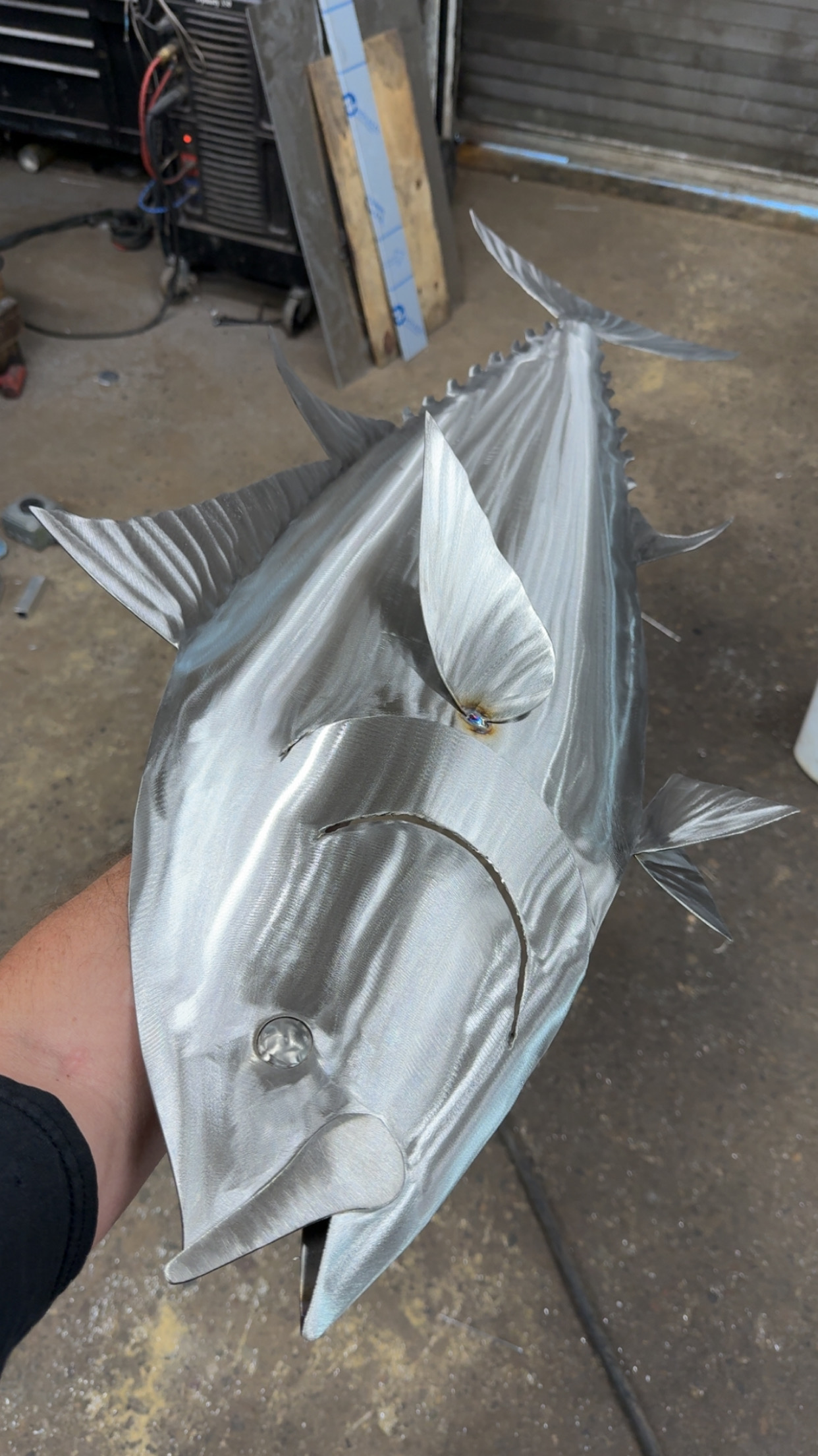 Polished aluminum tuna sculpture with hand-engraved detail held in the workshop