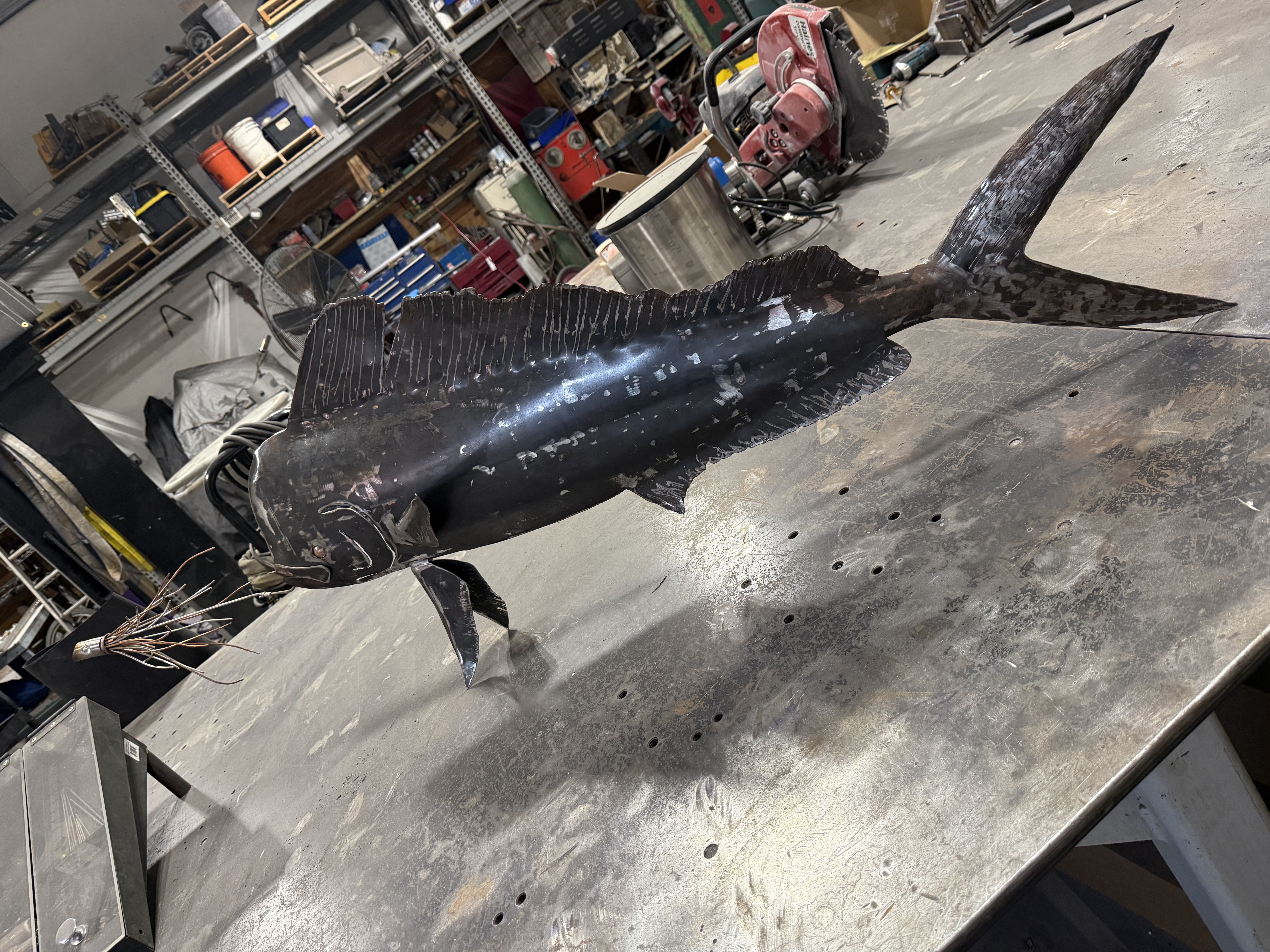 Handcrafted steel mahi-mahi sculpture with iridescent dark finish in the workshop